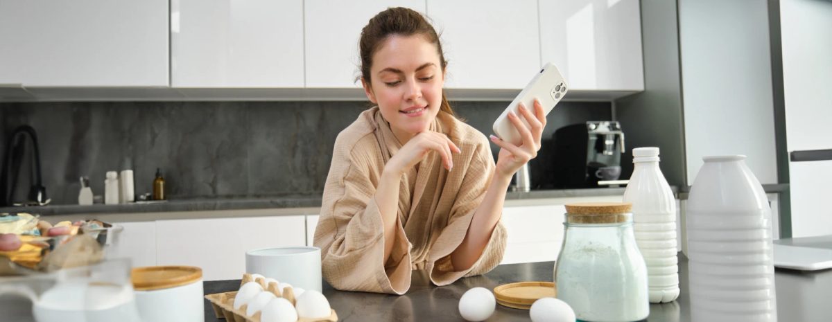 Home baker packing an order box with WhatsApp order messages visible on her phone
